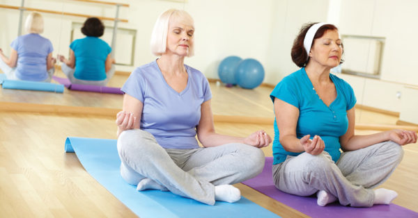 two older women in workout clothes sitting in a yoga room meditating