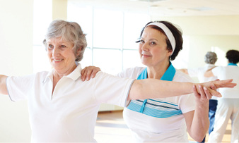 middle age woman trainer helping senior woman stretch arms and back