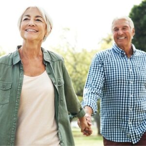 Older adult couple, woman and man walking hand-in-hand in the park.